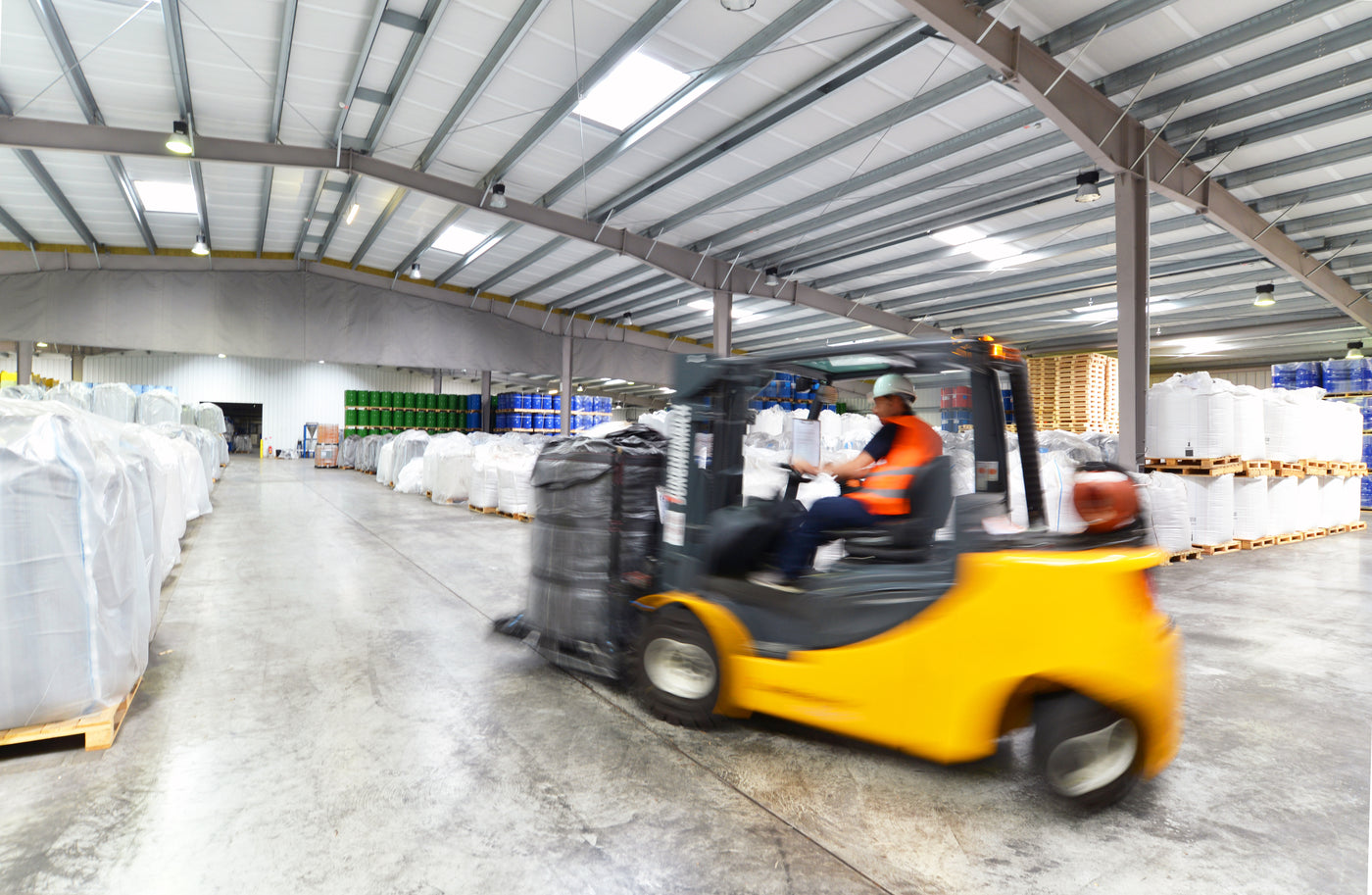 Worker operating a forklift in a warehouse with pallets and boxes.